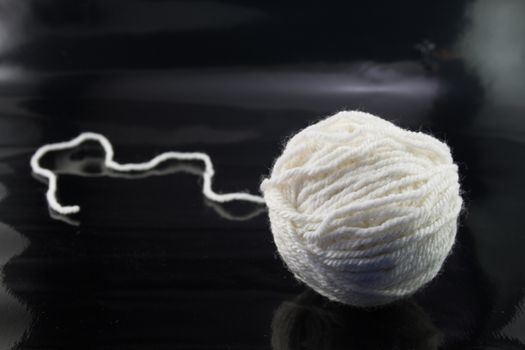 The white ball of wool thread on a black background, with the thread