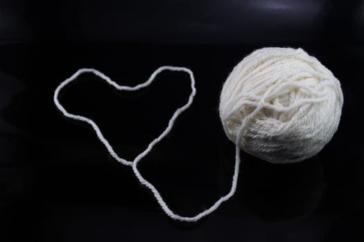 The white ball of wool thread on a black background, with the thread