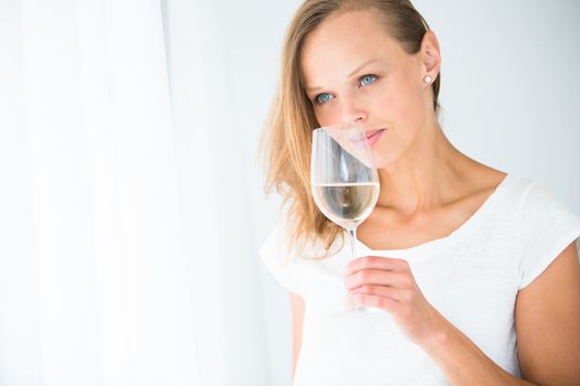 Gorgeous young woman with a glass of wine, smelling the lovely drink, savouring every sip (shallow DOF; color toned image)