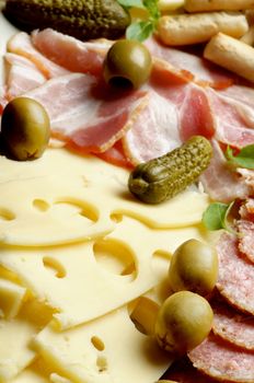 Arrangement Delicious Emmental Cheese with Smoked Meat, Green Olives and Gherkins closeup. Focus on Foreground