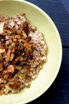 Delicious Homemade Buckwheat Stew with Roasted Bacon, Onion, Carrot and Bell Pepper closeup in Green Bowl on Wooden background. Top View