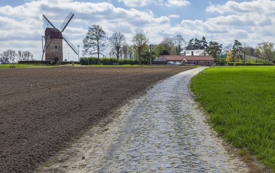 Cobbelstone road located in the North of France near Lille close to a traditional windmill (Moulin de Vertain). On such roads every year is organized one of the most famous one day cycling race Paris-Roubaix.