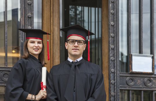 Portrait of a youg couple in the graduation day posing in front of the gate of the University.