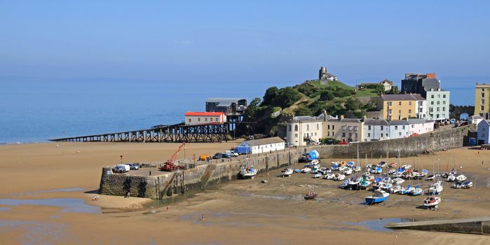 A view of Tenby harbour, in south Wales, with colourful, pastel houses overlooking the beach and sea, with the tide out