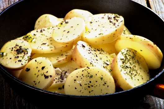 Wedges of Raw Potato with Basil, Salt and Olive Oil in Black Fry Pan closeup