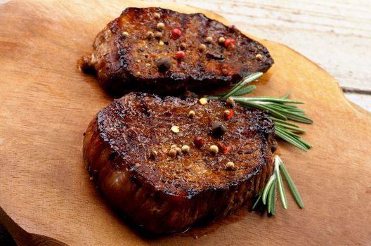 Delicious Roasted Beef Steaks with Spices and Rosemary on Wooden Plate on Rustic Wooden background
