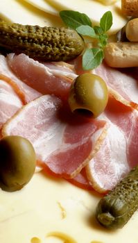 Background of Delicious Smoked Meat, Emmental Cheese, Green Olives and Gherkins closeup. Focus on Sliced Bacon