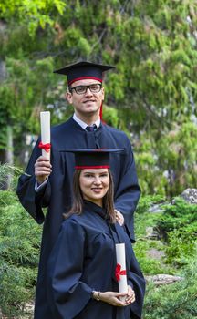 Young couple in the graduation day posing outdoor in a beautiful green garden.