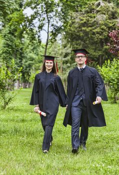 Young happy couple walking hand in hand in a green park in the graduation day.