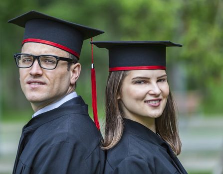 Outdoor portrait of a young couple of students in the graduation day in a park.