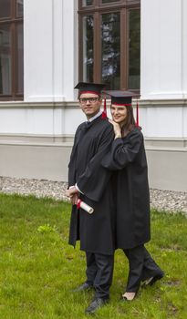Young couple in the gradutaion day posing outside in front of the University wall.