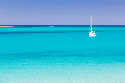 White sail boat at the beautiful turquoise blue mediterranean Pelosa beach near Stintino,Sardinia, Italy.