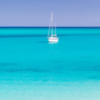 White sail boat at the beautiful turquoise blue mediterranean Pelosa beach near Stintino,Sardinia, Italy.