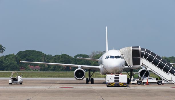 Two engine passenger jet airplane and airport vehicles at airport.