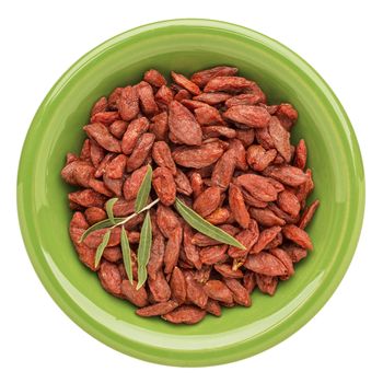 dried goji berries with a fresh leaf on an isolated green ceramic bowl