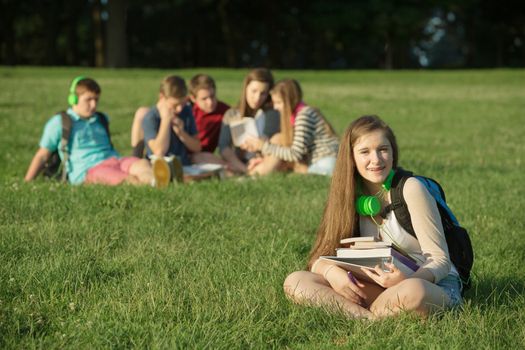 Cute female teenage student sitting near group outdoors