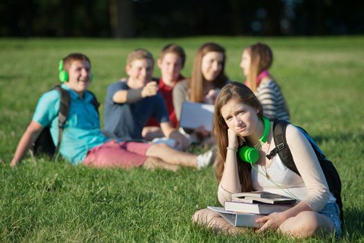 Pouting teen girl near group on grass outdoors