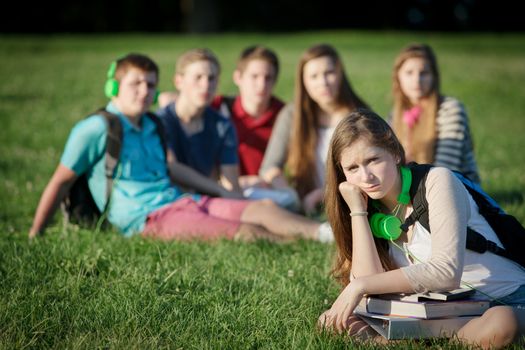Lonely female teen student sitting near group
