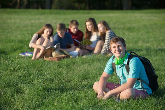 Confident male teen student with backpack sitting outdoors