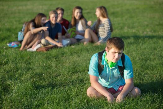 Depressed male teenage student sitting alone outdoors