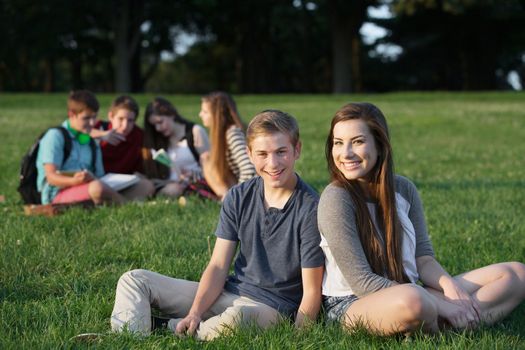 Two happy teenage male and female friends sitting outdoors