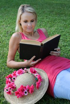 Pretty young woman reclining on the grass while reading a book