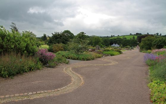 A wide path, with a snake like pattern, carving through manicured gardens, beneath a cloudy, grey sky