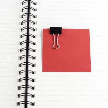 red paper note with black clip on notebook