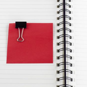 red paper note with black clip on notebook