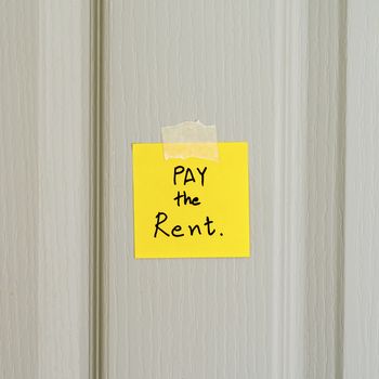 sticky note write a message pay the rent on wood door background