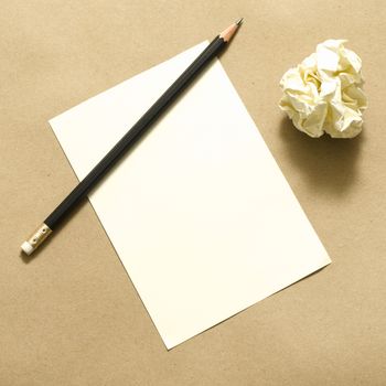 Pencil on clear white paper with crumble paper balls on brown color background