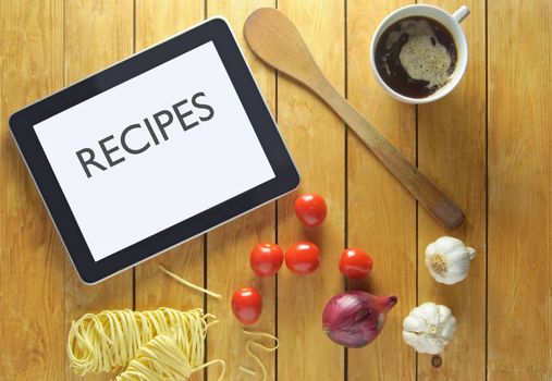 Tablet with recipes heading on a table surrounded by fresh food ingredients 