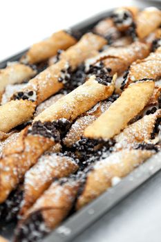 Tray full of freshly filled cannolis with chocolate chips and confectioners sugar. Shallow depth of field.