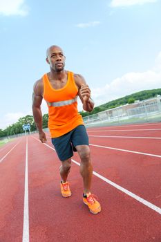 African American man in his 30s running at a sports track outdoors.