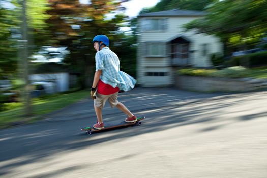 Action shot of a longboarder skating on an urban road. Slight motion blur from panning technique to capture movement.