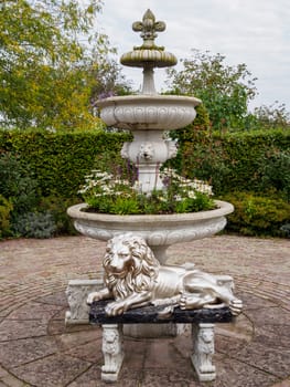 Lion statue lying down proud in front of a floral fountain