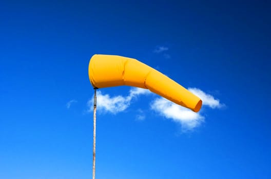 Yellow weather vane, wind sock, wind direction indicator against a blue sky.