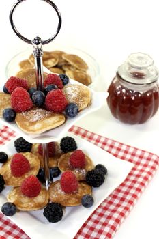 Poffertjes with berries and jelly on a cake stand on a light background