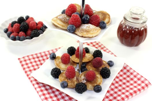 Poffertjes with berries on a cake stand on a light background