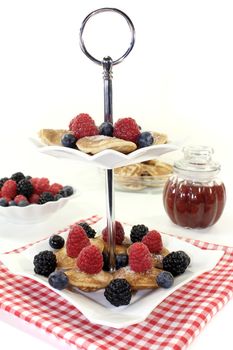 Poffertjes with blackberries on a cake stand on a light background