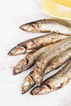 Culinary seafood eating. Grilled sardines on plate with lemon on white wooden background, top view.