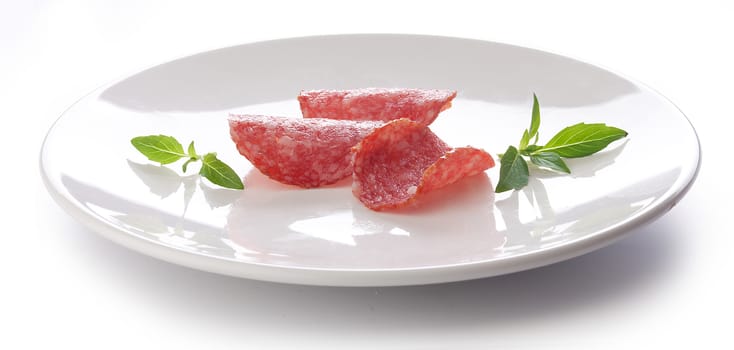 Three pieces of smoked sausage with fresh green basil on the white plate