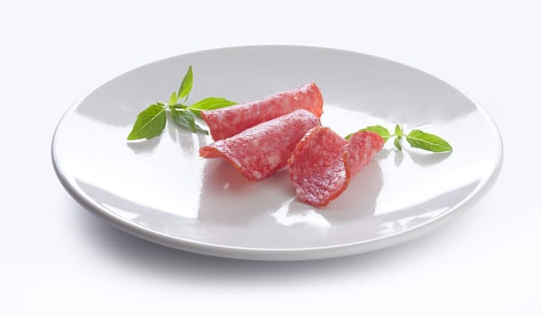 Three pieces of smoked sausage with fresh green basil on the white plate