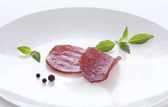 Two pieces of smoked sausage with fresh green basil and black pepper on the white plate