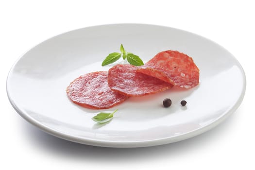 Three pieces of smoked sausage with fresh green basil and black pepper on the white plate