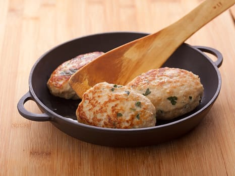 Black frying pan with three meat rissoles on the wooden table