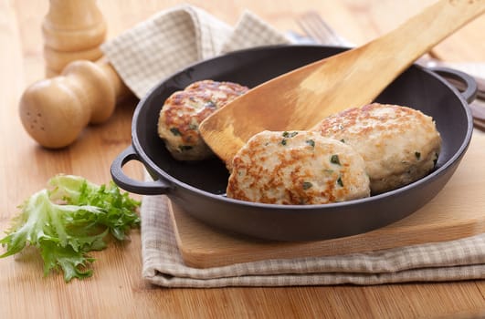 Black frying pan with three meat rissoles on the kitchen table