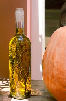 Still life on a wooden surface of the table is a bottle with olive oil and spices inside the bottle. It is next to the pumpkin.