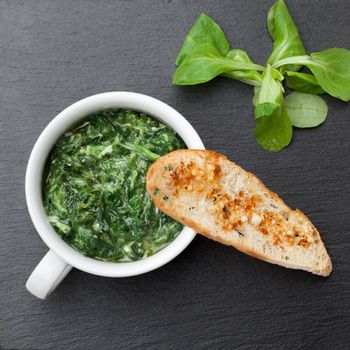 Appetizer sauteed garlic spinach dish in cup, baked bread slice  with  melted cheese served on black stone