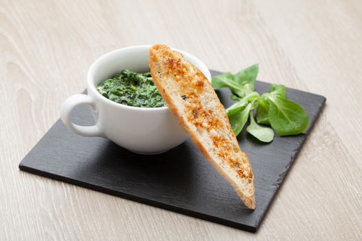 Appetizer sauteed garlic spinach dish in cup, baked bread slice  with  melted cheese served on black stone